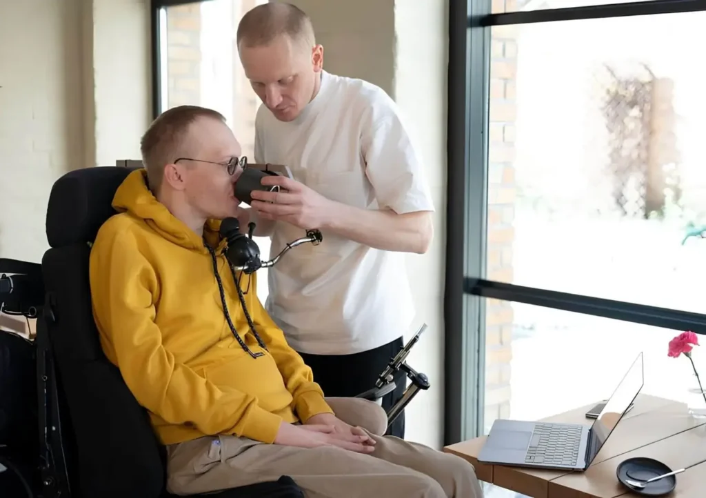 Friendly NDIS support worker helping a person in his wheelchair drink a glass of water providing aged care and disability support in Australia